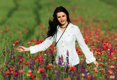Beautiful young woman standing by flowers on field