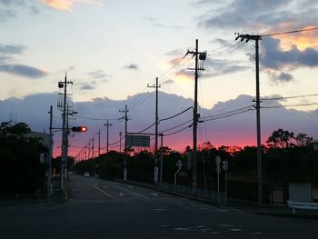 Road by silhouette trees against sky during sunset