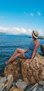 Woman sitting on rock at beach against sky