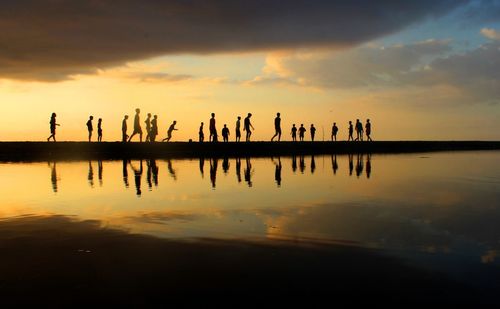 Silhouette people on lake against sky during sunset