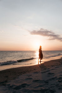 Silhouette woman walking at beach against sky during sunset
