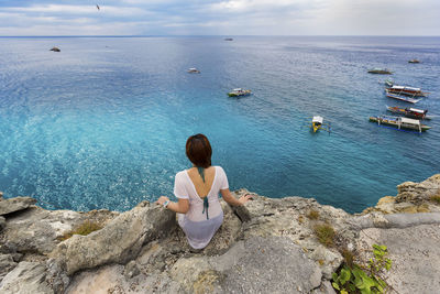 Rear view of woman sitting on rock by sea