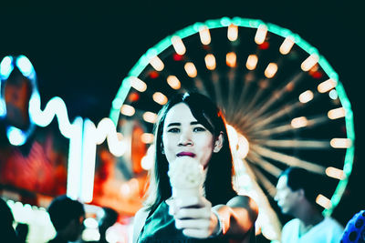 Portrait of smiling young woman standing holding ice cream in city at night