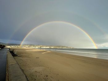 Scenic view of beach against rainbow in sky
