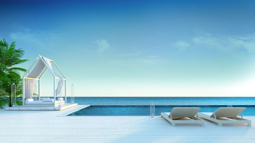 Lounge chairs by swimming pool at beach against blue sky