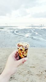 Cropped image of person hand holding taho at beach against sky