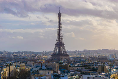 Tower and buildings in city against cloudy sky