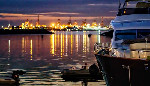 Boats moored at illuminated harbor against sky at sunset