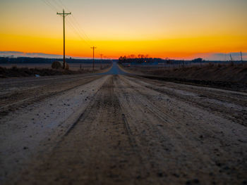 Surface level of road amidst field against sky during sunset