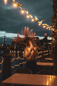 Young woman tossing hair while holding illuminated lighting equipment at night