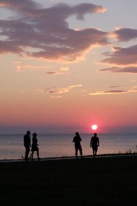 Silhouette people on beach against sky during sunset