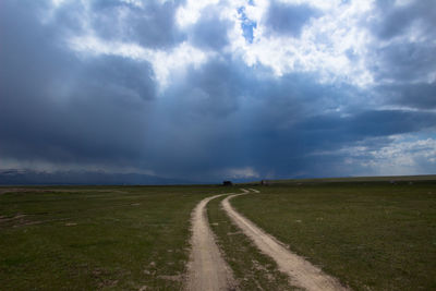 Road amidst field against sky during rainy season