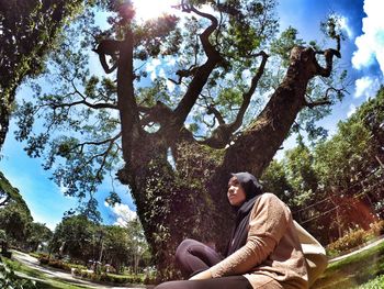 Fish-eye view of woman sitting against tree at park on sunny day