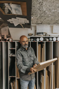 Bald mature owner wearing eyeglasses analyzing picture frame in workshop