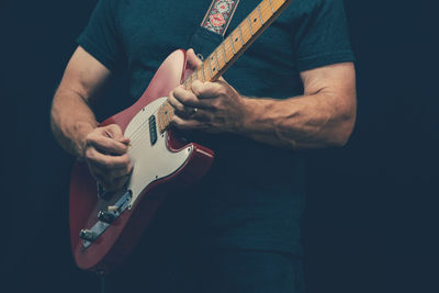 Midsection of man playing guitar against black background