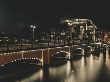 Illuminated bridge over river in city against sky at night