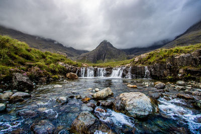 Scenic view of water flowing through rocks against sky