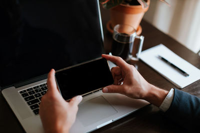 Midsection of man using mobile phone by laptop in office