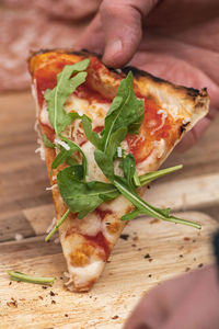 Hand taking last piece or slice of pizza with tomato sauce, mozzarella and fresh rocket leaves
