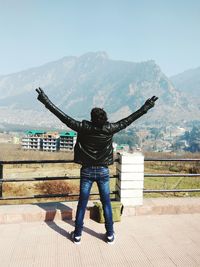 Rear view of man with arms outstretched against mountain range