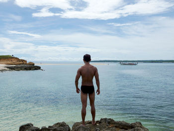 Rear view of shirtless man looking at sea against sky