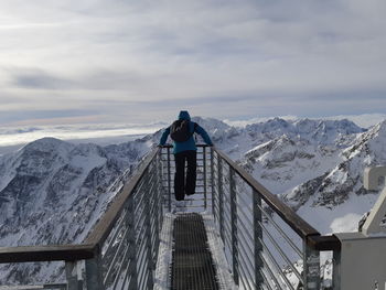 Rear view of man looking at snowcapped mountains while standing on observation point against sky