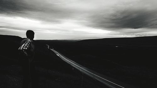 Rear view of man standing on mountain against sky