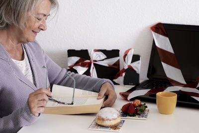 Smiling senior woman reading book while sitting at table