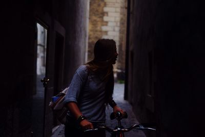 Young woman looking away while holding bicycle on street