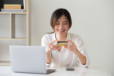 Young woman using phone while sitting on laptop