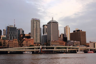 Modern buildings by river against sky in city