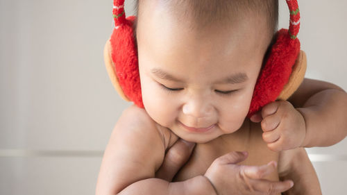 Cropped image of hands holding cute baby boy wearing ear muff against wall