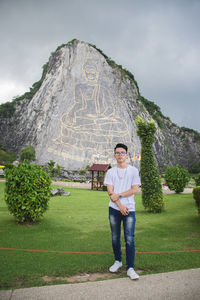 Portrait of young man standing against buddha carving mountain 