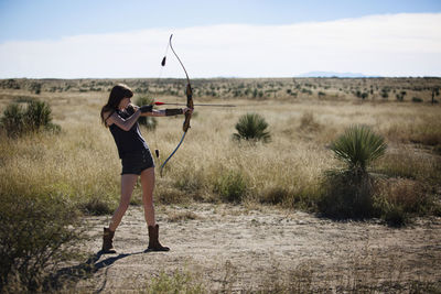 Woman aiming with bow and arrow while standing on field