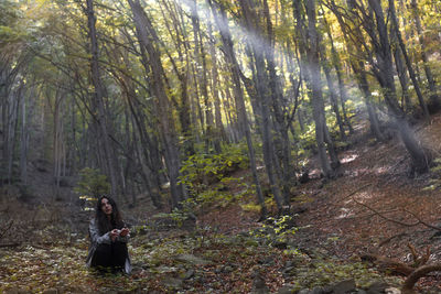 Woman standing by tree trunks in forest