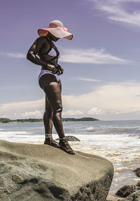 Rear view of woman standing at beach against sky