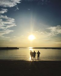 Silhouette people on beach against sky during sunset