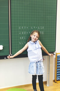 Portrait of smiling girl standing against blackboard in classroom at school