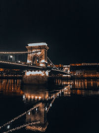 Illuminated bridge over river against sky at night