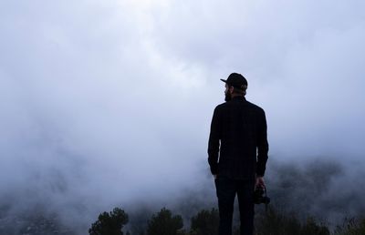 Rear view of man standing against sky during foggy weather