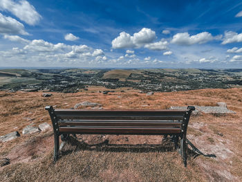 Empty bench on field against sky