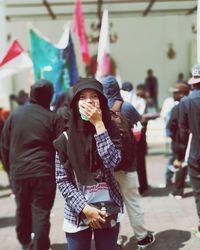 Portrait of young woman covering mouth while standing on street in city