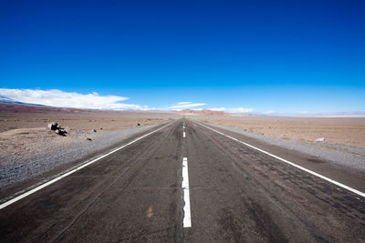 Road passing through desert against blue sky
