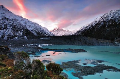 Scenic view of lake by snowcapped mountains against sky during sunset