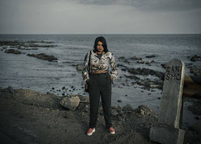 Woman standing on rock at beach against sky