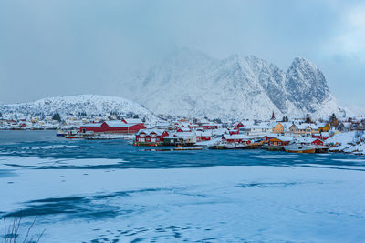Scenic view of snowcapped mountains by town against sky during winter
