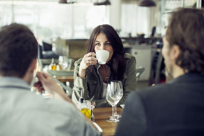 Mature woman drinking coffee while looking at colleague during lunch meeting in restaurant