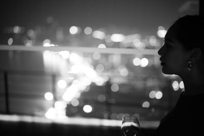 Side view of beautiful woman with wineglass against illuminated city at night