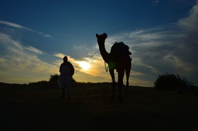 Silhouette men standing on field against sky during sunset