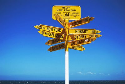 Information sign by sea against clear blue sky
